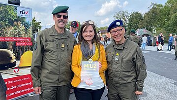 Eine Dame hält den Miliz Award 2021 in den Händen. Links und rechts von ihr je ein uniformierter Mann.