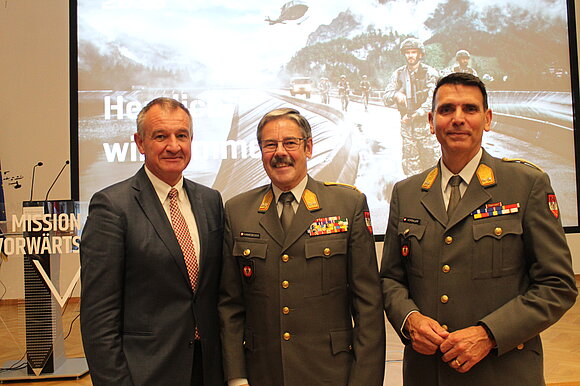 Gruppenfoto: zwei Herren in Uniform, ein Herr im Anzug.